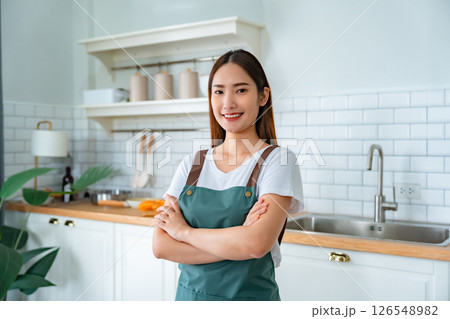 Happy young asian woman wearing apron and standing in kitchen room 126548982