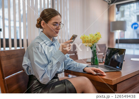 Woman Phone Laptop Young woman uses phone at desk indoors during work for communication. 126549438