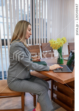 Woman Laptop Business: Blonde works on laptop at table in office, daytime, focused on career task. Woman Laptop Business: Blonde works on laptop at table in office, daytime, focused on career task. 126549447