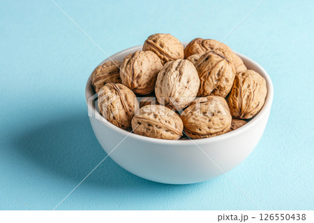 A white bowl filled with walnuts sits on a light blue background.  126550438