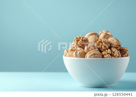 A white bowl filled with walnuts sits on a light blue background. A white bowl filled with walnuts sits on a light blue background. 126550441