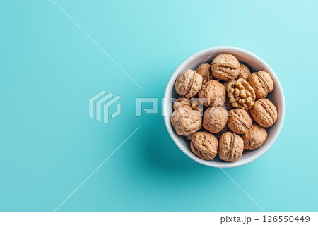 A white bowl filled with walnuts sits on a light blue background. A white bowl filled with walnuts sits on a light blue background. 126550449
