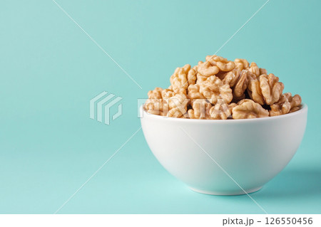 A white bowl filled with walnuts sits on a light blue background.  126550456