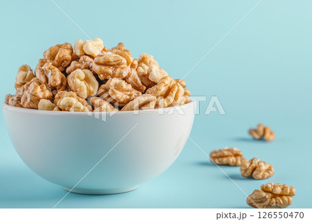 A white bowl filled with walnuts sits on a light blue background.  126550470