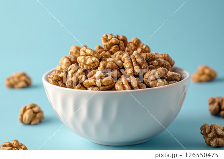 A white bowl filled with walnuts sits on a light blue background.  126550475