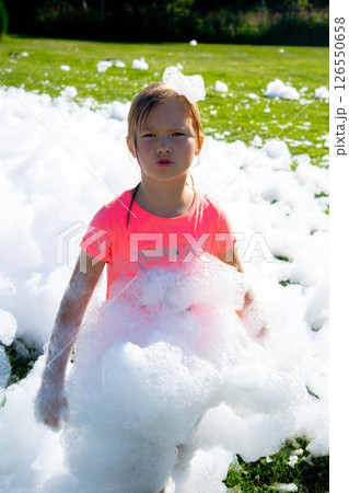 Young girl playing in outdoor foam party with pink shirt and bubbles 126550658