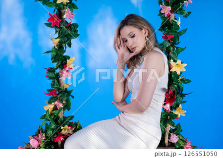 An Elegant Portrait Featuring a Beautiful Model on a Floral Swing Against a Blue Sky Background An Elegant Portrait Featuring a Beautiful Model on a Floral Swing Against a Blue Sky Background 126551050
