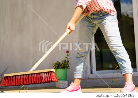 Woman using broom to clean up backyard patio Woman using broom to clean up backyard patio 126554865