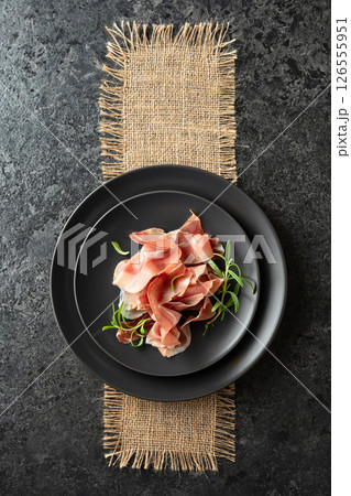 Prosciutto and rosemary on a black table. 126555951