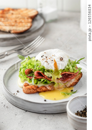 Toasted bread with poached egg, salad, cheese and ham on a plate on white kitchen background. Healthy breakfast, diet food Toasted bread with poached egg, salad, cheese and ham on a plate on white kitchen background. Healthy breakfast, diet food 126556834