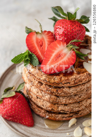 Oatmeal belgian waffles with strawberry, honey and almond petals stacked on a plate close up, white background 126556860