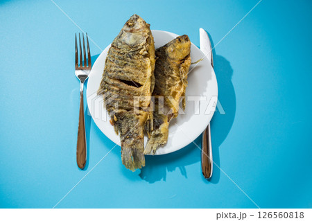 Fried crucian carp with a crispy golden crust on a white plate 126560818