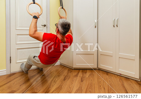 Man exercises with gymnastic rings at home during morning Man exercises with gymnastic rings at home during morning 126561577