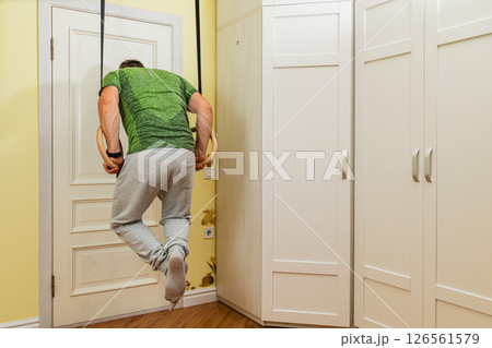 Man exercises on gymnastic rings in a home setting Man exercises on gymnastic rings in a home setting 126561579
