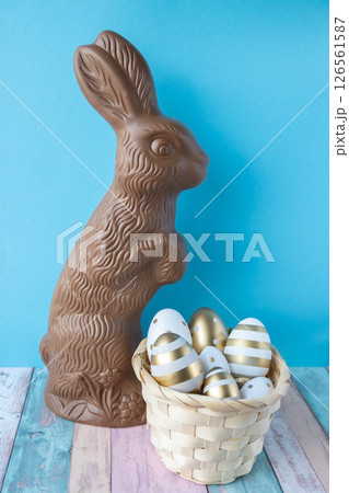 Chocolate in form of Easter rabbit on a blue background and basket with eggs. 126561587