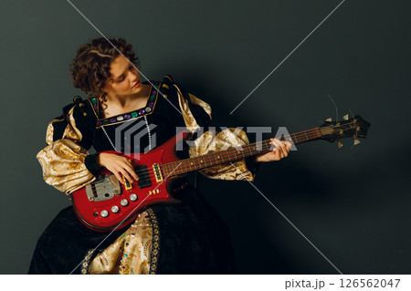 Portrait of a young adult woman playing classical music on electric guitar and dressed in a medieval dress 126562047