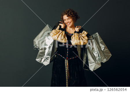 Portrait of a young adult woman dressed in a medieval dress holding shopping bags in hands 126562054