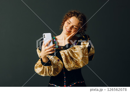 Portrait of a young aristocratic woman holding mobile phone dressed in a medieval dress on dark background Portrait of a young aristocratic woman holding mobile phone dressed in a medieval dress on dark background 126562078