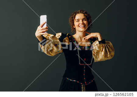 Portrait of a young aristocratic woman holding mobile phone dressed in a medieval dress on dark background Portrait of a young aristocratic woman holding mobile phone dressed in a medieval dress on dark background 126562105