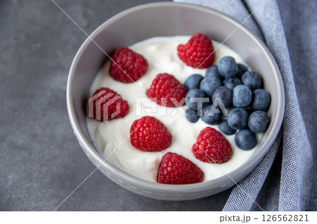 Natural fresh greek yogurt with raspberry, blueberry berries in dark plate and napkin for healthy breakfast. Natural fresh greek yogurt with raspberry, blueberry berries in dark plate and napkin for healthy breakfast. 126562821