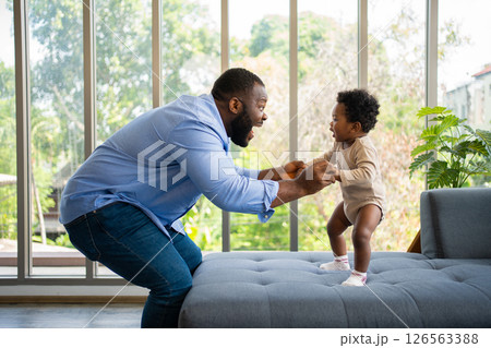 Portrait Of Happy African American Dad With Cute Little Baby Girl on couch at home in the living room, caring father smiling and amusing his girl while sitting on the couch, happy family Portrait Of Happy African American Dad With Cute Little Baby Girl on couch at home in the living room, caring father smiling and amusing his girl while sitting on the couch, happy family 126563388