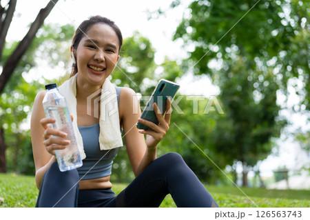 Asian young women drink water from a plastic bottle after exercises or sports. Asian woman running in garden. Beautiful fitness athlete woman drinking pure water after workout exercise on morning Asian young women drink water from a plastic bottle after exercises or sports. Asian woman running in garden. Beautiful fitness athlete woman drinking pure water after workout exercise on morning 126563743