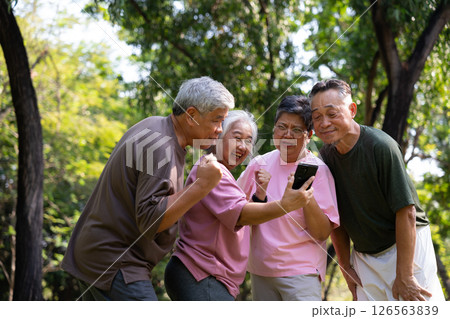 Group of happy Senior Retirement Using Smartphone and laughing outdoors at the park after a workout and spending time together, concepts about the elderly, seniority, and wellness aging 126563839