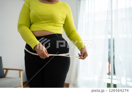 Overweight woman using a tape measure around waist and belly fat, Fat Asian woman workout at home. Concept of healthy, food for health and lifestyle, weight loss Overweight woman using a tape measure around waist and belly fat, Fat Asian woman workout at home. Concept of healthy, food for health and lifestyle, weight loss 126564274