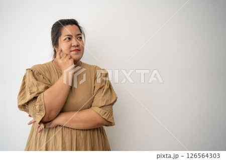 Thoughtful Woman in Beige Dress: A plus-size woman in a stylish beige dress, thoughtfully touches her temple, lost in contemplation. 126564303