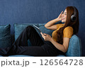 Relaxed young Asian woman in headphones listening to online music media entertainment on smartphone, relaxing on sofa at home. Flat rest relax spend free spare time in the living room. Lounge concept 126564728