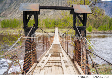 Wooden suspension footbridge crossing Chulyshman river near Katu Yaryk pass Altai Russia Remote connection point in wild mountain region Wooden suspension footbridge crossing Chulyshman river near Katu Yaryk pass Altai Russia Remote connection point in wild mountain region 126567298