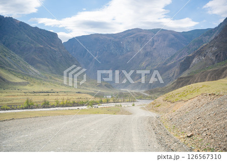 Gravel road running along Chulyshman river in mountain valley Altai Russia Remote travel route through scenic wilderness Gravel road running along Chulyshman river in mountain valley Altai Russia Remote travel route through scenic wilderness 126567310