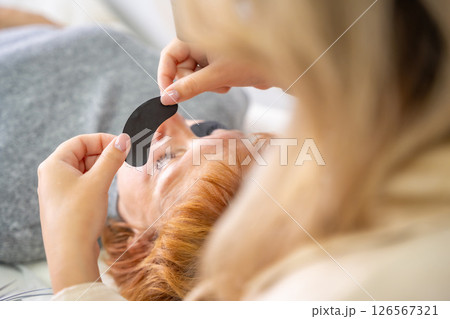Close-up of beautician hands holding black under-eye patch before UV eyelash extension. Professional tools preparation for modern lash enhancement technique. 126567321