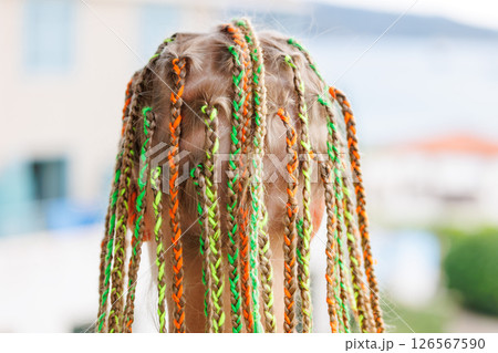 Back view cute blonde girl with colorful braided hair on sunny day seaside beach coast vacation. She stands balcony seaside resort joyful holiday vibe. Carefree little child stylish summer hairstyle Back view cute blonde girl with colorful braided hair on sunny day seaside beach coast vacation. She stands balcony seaside resort joyful holiday vibe. Carefree little child stylish summer hairstyle 126567590