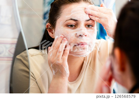 Young adult practicing skincare with foaming cleanser at sink. Ideal for Gen Z beauty trends or teen hygiene education. Young adult practicing skincare with foaming cleanser at sink. Ideal for Gen Z beauty trends or teen hygiene education. 126568579