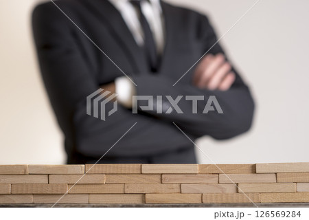 Businessman with folded arms with wall of wooden bricks infront of him 126569284