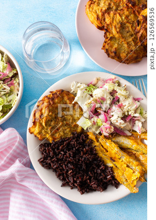 A wholesome and savory breakfast with brown rice and baked white fish, complemented by zucchini-carrot pancakes and a fresh Chinese cabbage salad with radish 126569536