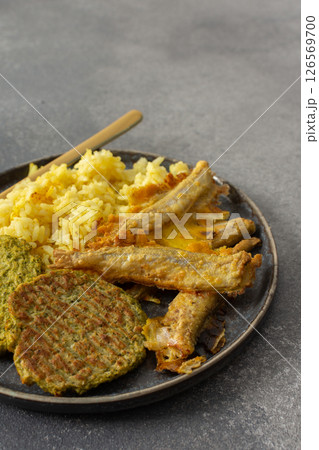 A wholesome breakfast featuring turmeric rice with baked ocean fish, complemented by broccoli pancakes and roasted vegetables, offering a nutritious and satisfying meal 126569700