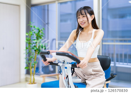 自宅の部屋でフィットネスバイクで運動する女性　家　エアロバイク　運動 126570830