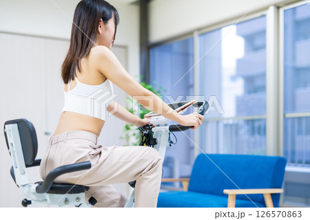 自宅の部屋でフィットネスバイクで運動する女性　家　エアロバイク　運動 126570863