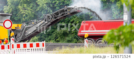 Asphalt milling and grinding machine at road repair and construction site throwing shredded old bitumen in big industrial heavy dumper tipper truck for recycling. Highway renewal with heavy machinery 126571524