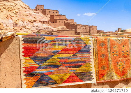 Colorful traditional carpets gifts selling on the market streets of ancient Ait Benhaddou ksar village, Ouarzazate province, Morocco Colorful traditional carpets gifts selling on the market streets of ancient Ait Benhaddou ksar village, Ouarzazate province, Morocco 126571730