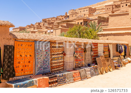 Colorful traditional carpets and other gifts selling on the market streets of ancient Ait Benhaddou ksar village, Ouarzazate province, Morocco Colorful traditional carpets and other gifts selling on the market streets of ancient Ait Benhaddou ksar village, Ouarzazate province, Morocco 126571733