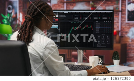 Day trader using PC to purchase and sell stocks, reading files, aiming to capitalize on market trends and fluctuations. Investor tracking stock forex trends on computer monitor, camera B 126572390