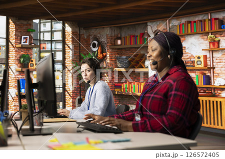 Call center agent laughing at funny joke while talking with customer in office. Customer service representative amused by comical conversation with client while providing assistance Call center agent laughing at funny joke while talking with customer in office. Customer service representative amused by comical conversation with client while providing assistance 126572405