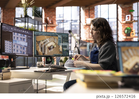 Freelancer designer decorates an apartment floor plan on a computer, using architectural software to configure elements. Woman uses interface to enable rendering and 3D modeling. 126572416