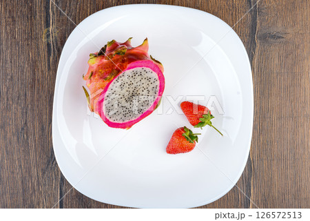 Top view of a white plate with half a pitahaya and two strawberries. 126572513