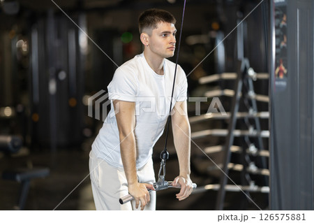 In gym, man uses cable row machine to strengthen muscles. In gym, man uses cable row machine to strengthen muscles. 126575881