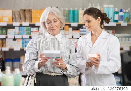 Elderly woman choosing packages of pills and medicines with pharmacist at pharmacy 126576103