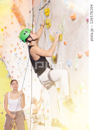 Positive extreme young guy with rope training on concrete climbing rock wall to maintain healthy discipline in indoor adventure park 126576104